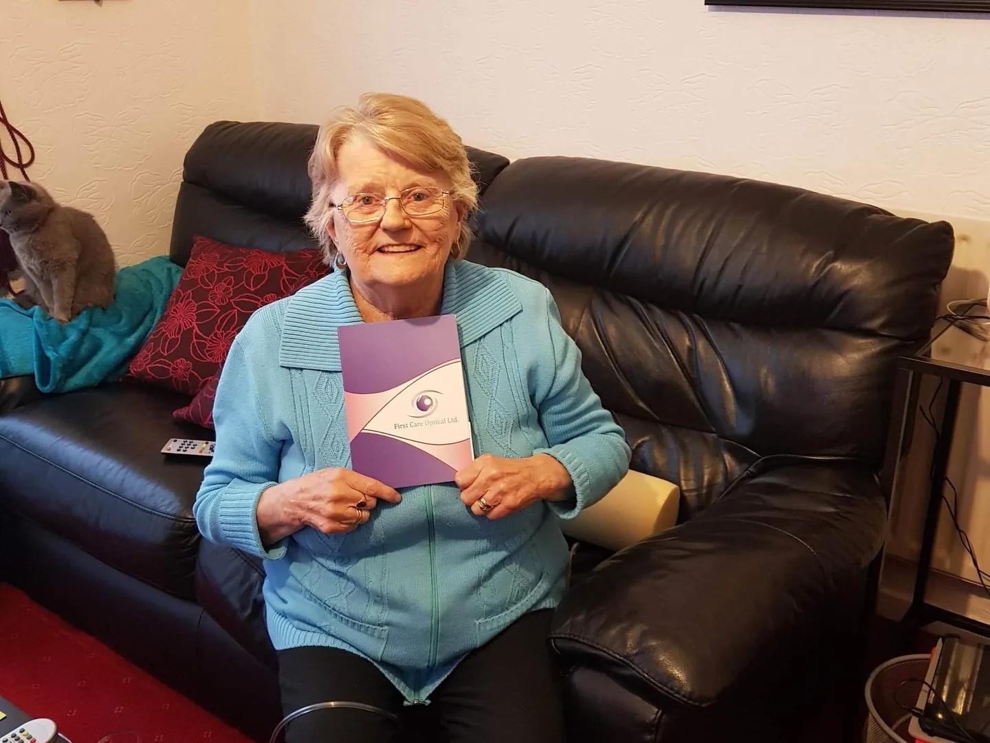 Smiling older patient at home holding her First Care Optical folder after a home eye test